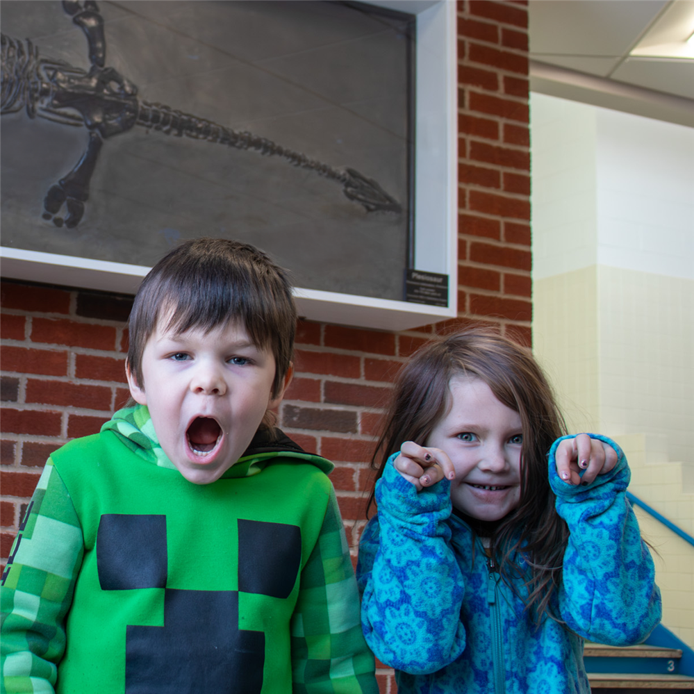  Students make dinosaur faces in front of a newly-donated plesiosaur fossil